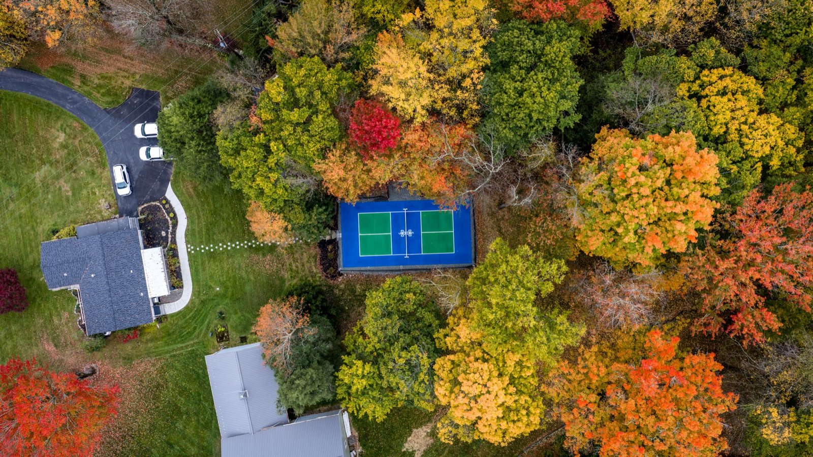 Wooded property and sport court in peak fall color from above
