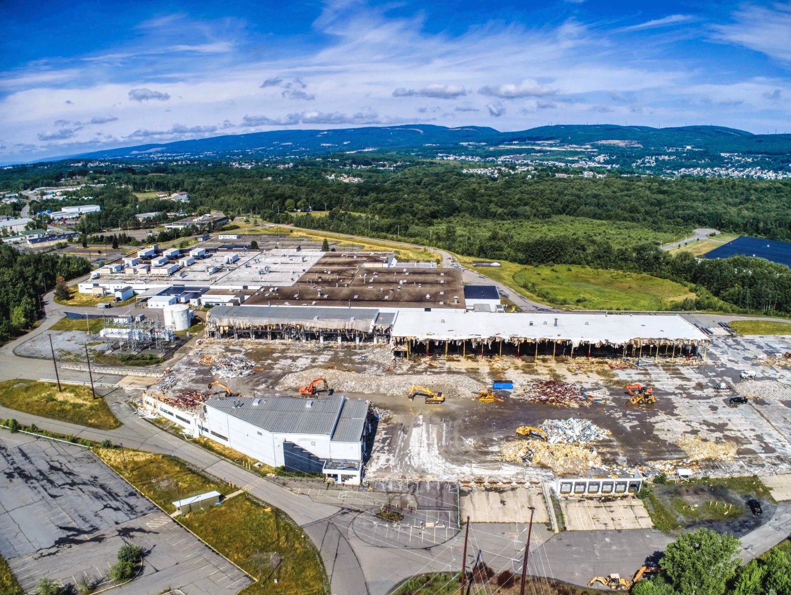 Large commercial site under demolition and construction, with heavy equipment and the mountains beyond