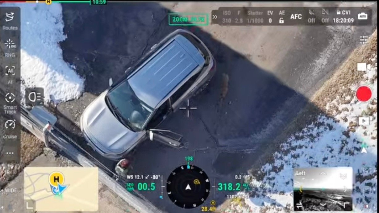 Drone camera view from a recent pet search: a pet beside a car with its door open in a snowy lot