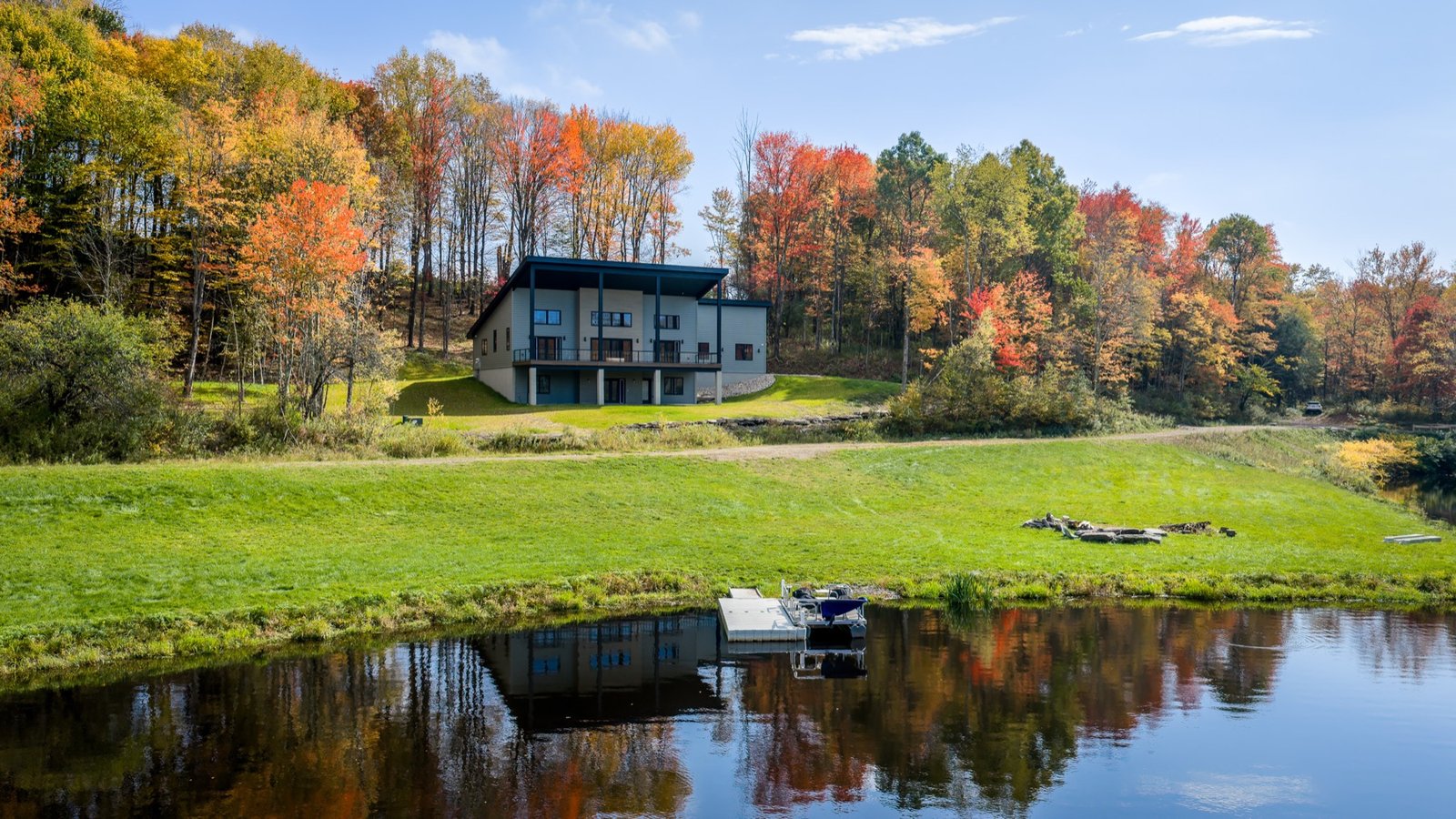 New construction home above a private lake, with fall trees reflected in the water